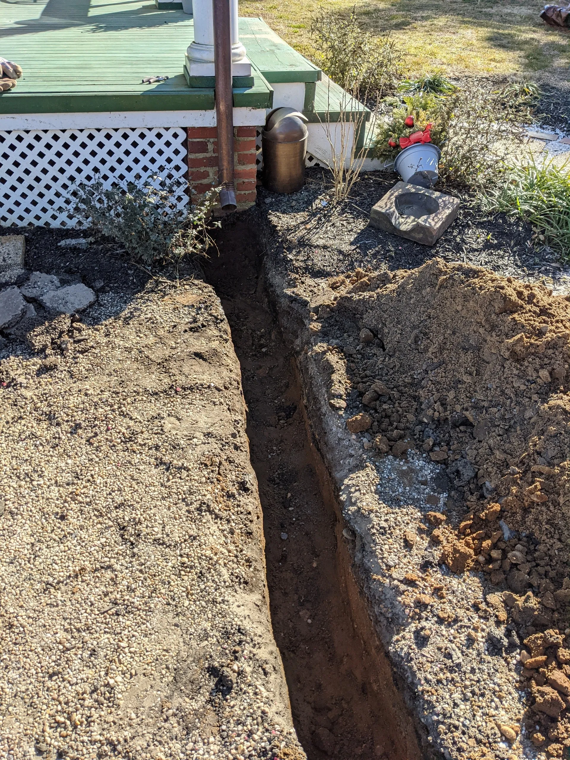 Deep trench dug alongside a porch foundation and a gravel path