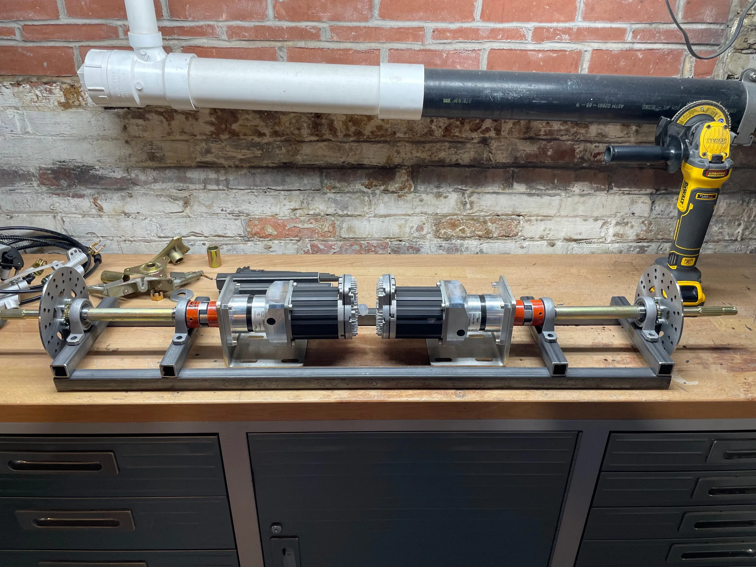 Both drive assemblies mounted facing outward on a rectangular steel frame, on a workbench under a brick wall