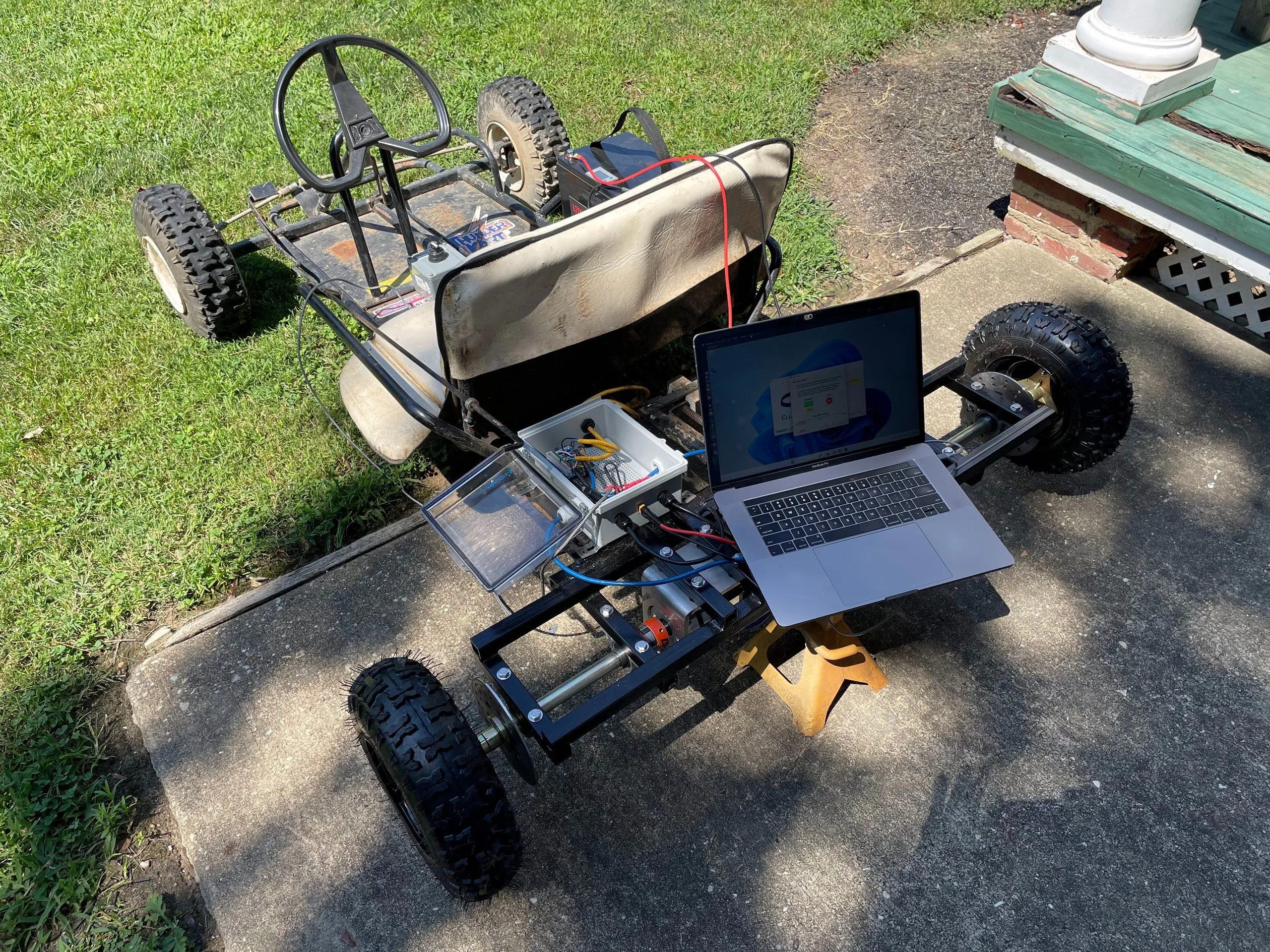 The go-kart parked on grass with a laptop propped on the rear subframe, connected to the motors