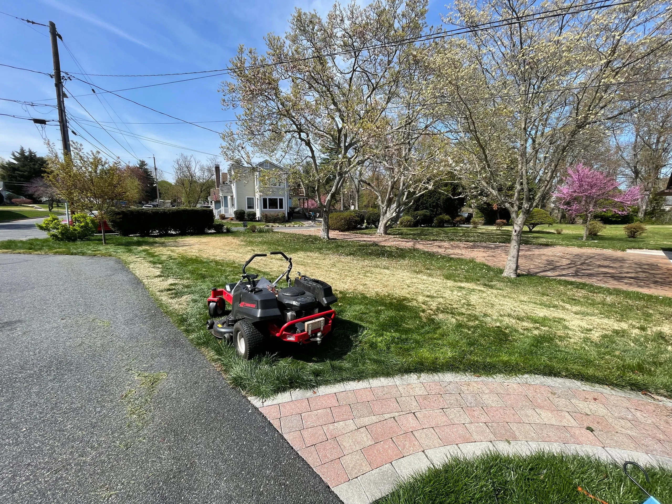 The mower parked on the front lawn beside the driveway, with mowed stripes visible across the grass and the street and neighboring houses behind
