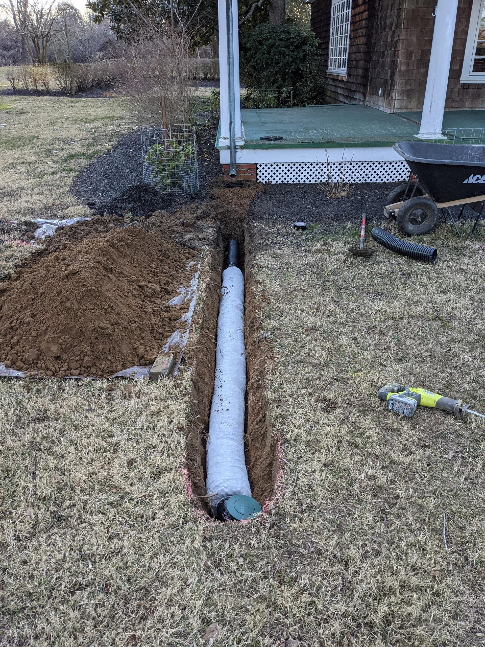 Trench near a side porch with sock-wrapped pipe connected to a pop-up emitter, most of the run backfilled
