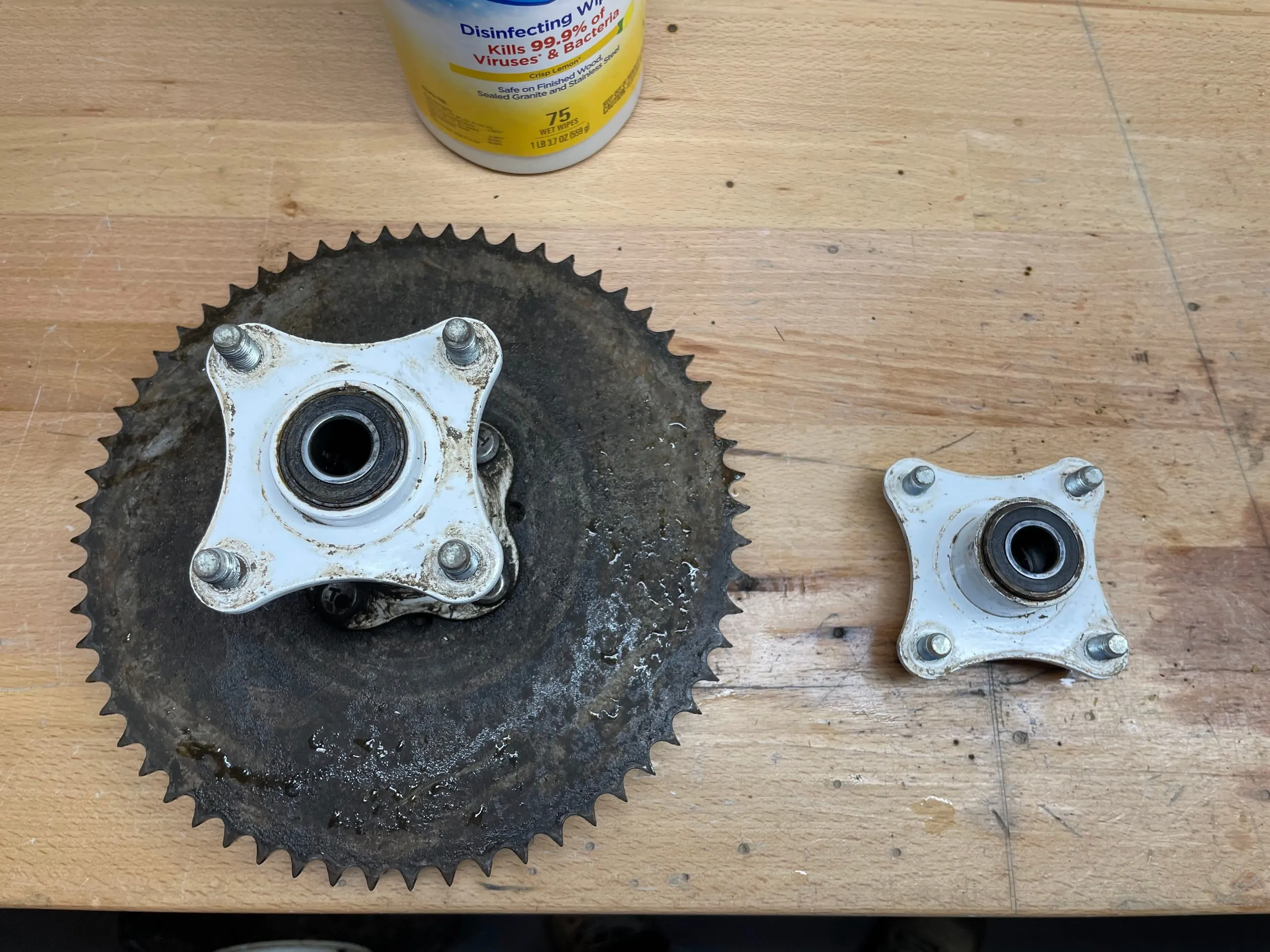 A greasy 60-tooth sprocket with a wheel hub bolted through it, beside a second bare wheel hub, on a workbench