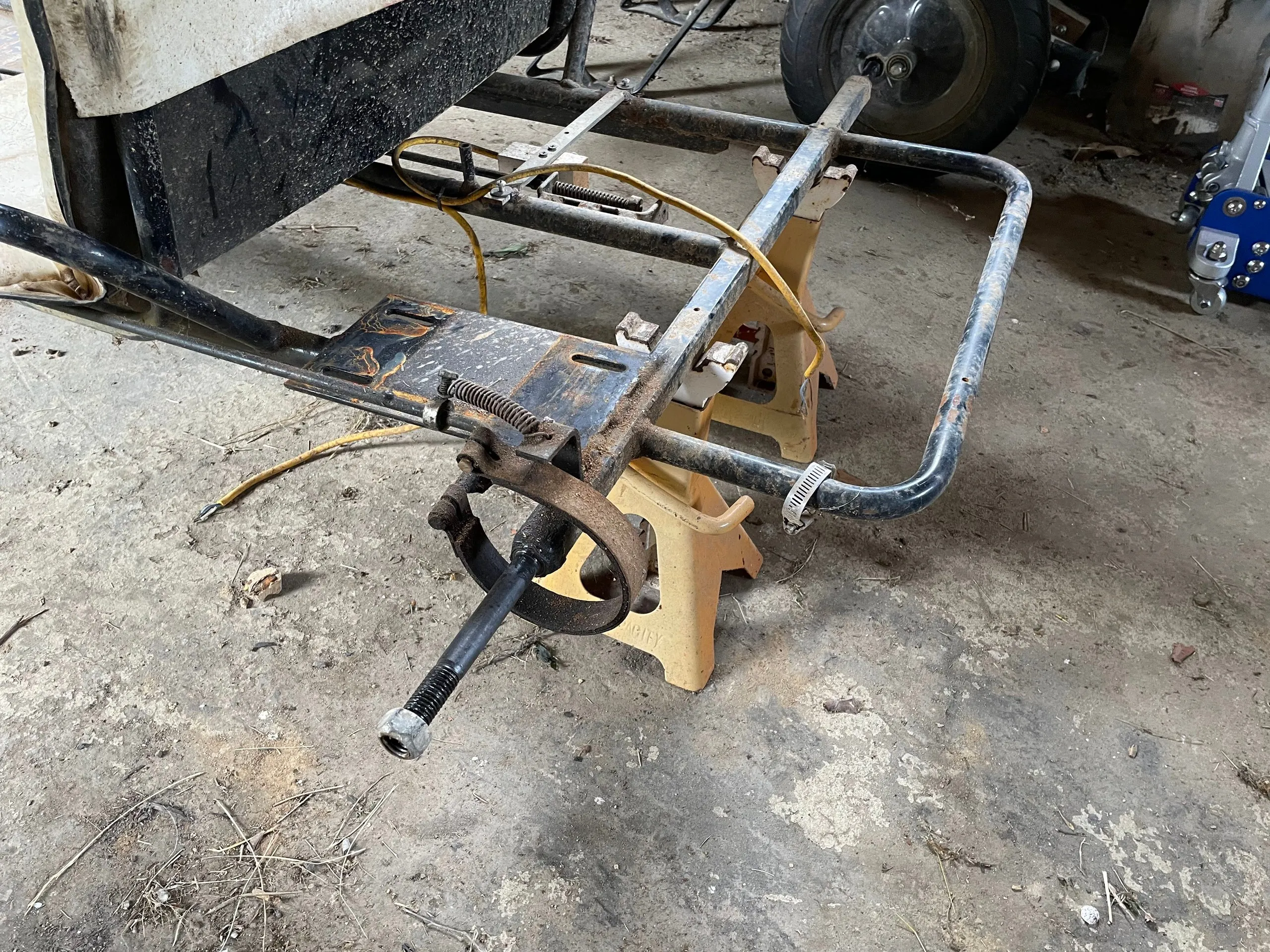 Close view of the rear frame rail showing the band brake, threaded axle stub and yellow throttle cable