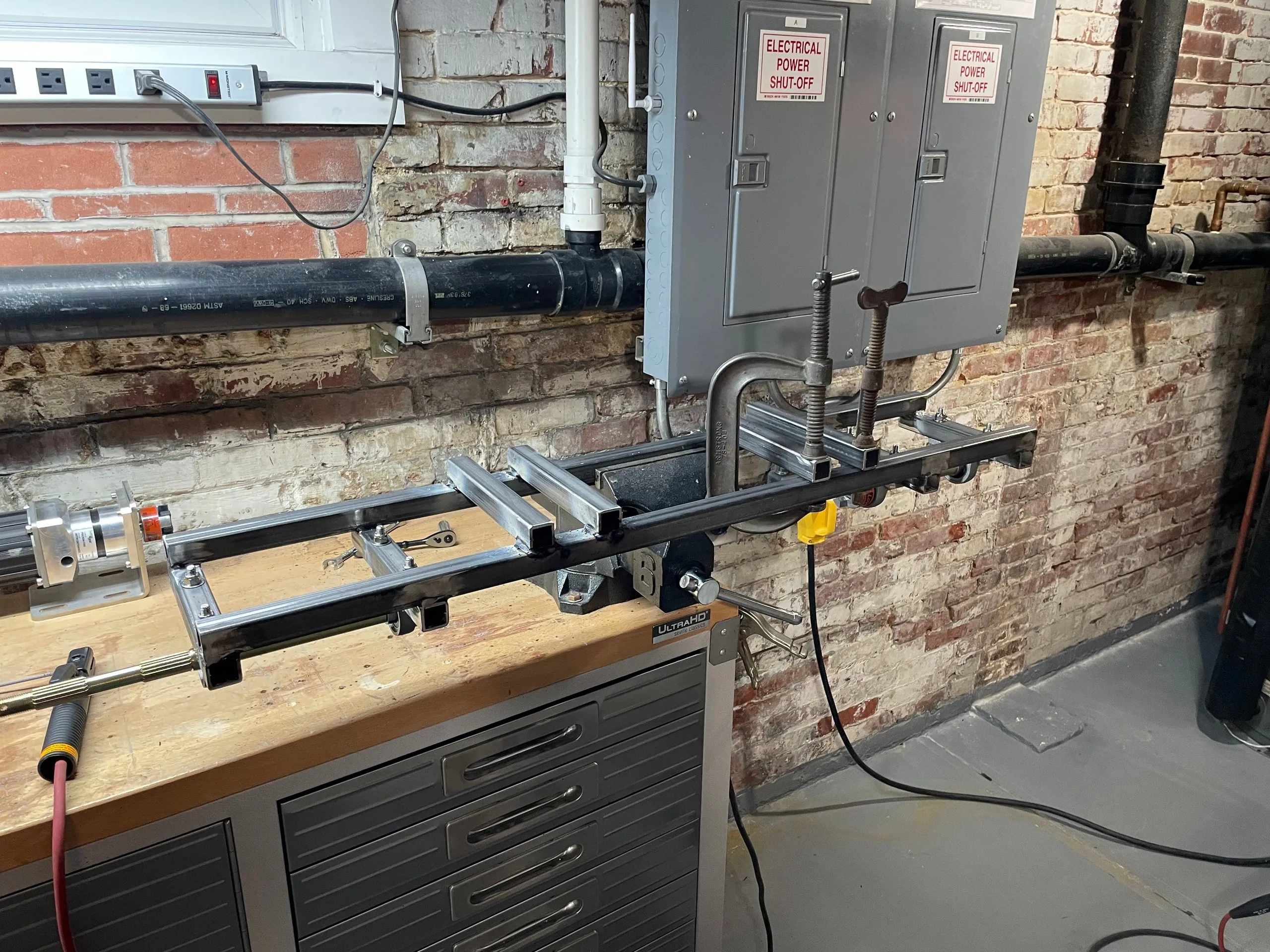 A square-tube subframe clamped in a bench vise with one drive assembly fitted at the far end