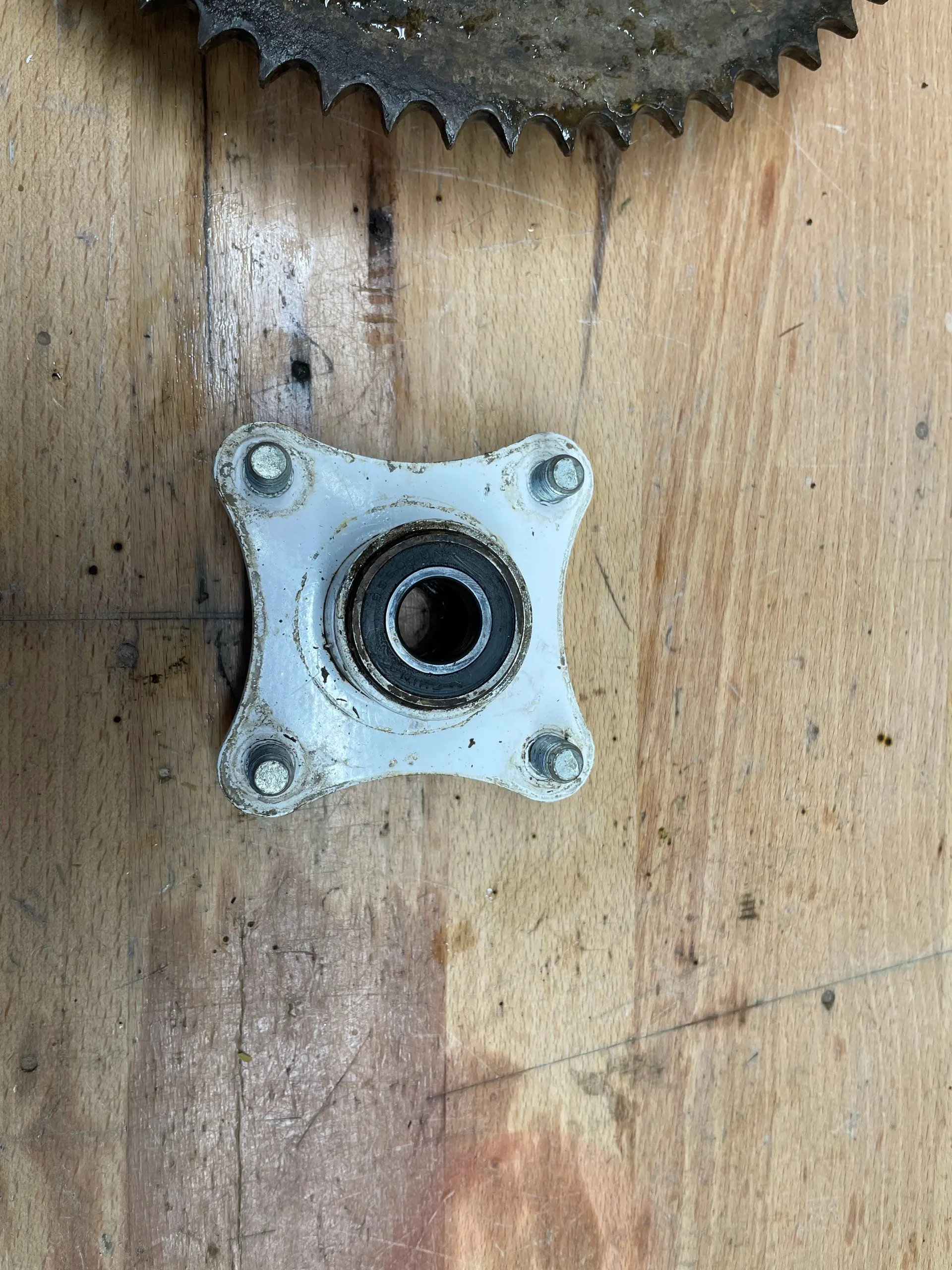 A white painted four-bolt wheel hub with a bearing pressed into its centre, lying on a workbench